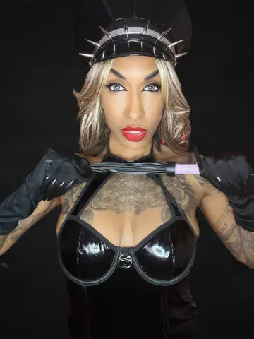 Glamorous woman in black latex outfit and spiked headpiece posing against a dark background.