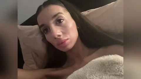 DeviNessa rests her head on a light pink pillow with long dark hair falling over her shoulders.