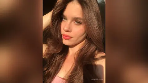 Young woman with long brown hair posing in warm sunlight for a soft, glowing portrait.
