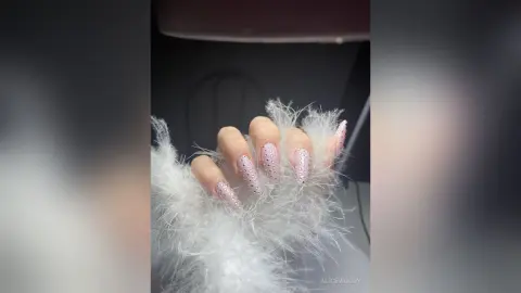 Close-up of elegant long almond-shaped nails with pink glitter design held by soft white faux fur trim.