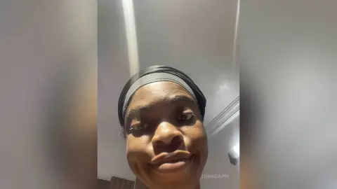 Smiling young woman in a black headwrap posing for a selfie in a bright indoor setting.