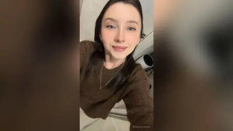 Smiling young woman in a cozy brown knit sweater posing in a bright indoor setting.