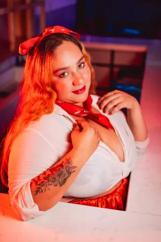Smiling woman in a white blouse and red headscarf posing in warm, moody red lighting.