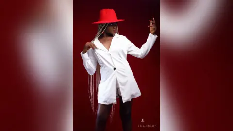 Stylish woman in a white button-down shirt and red wide-brimmed hat posing against a red studio background.