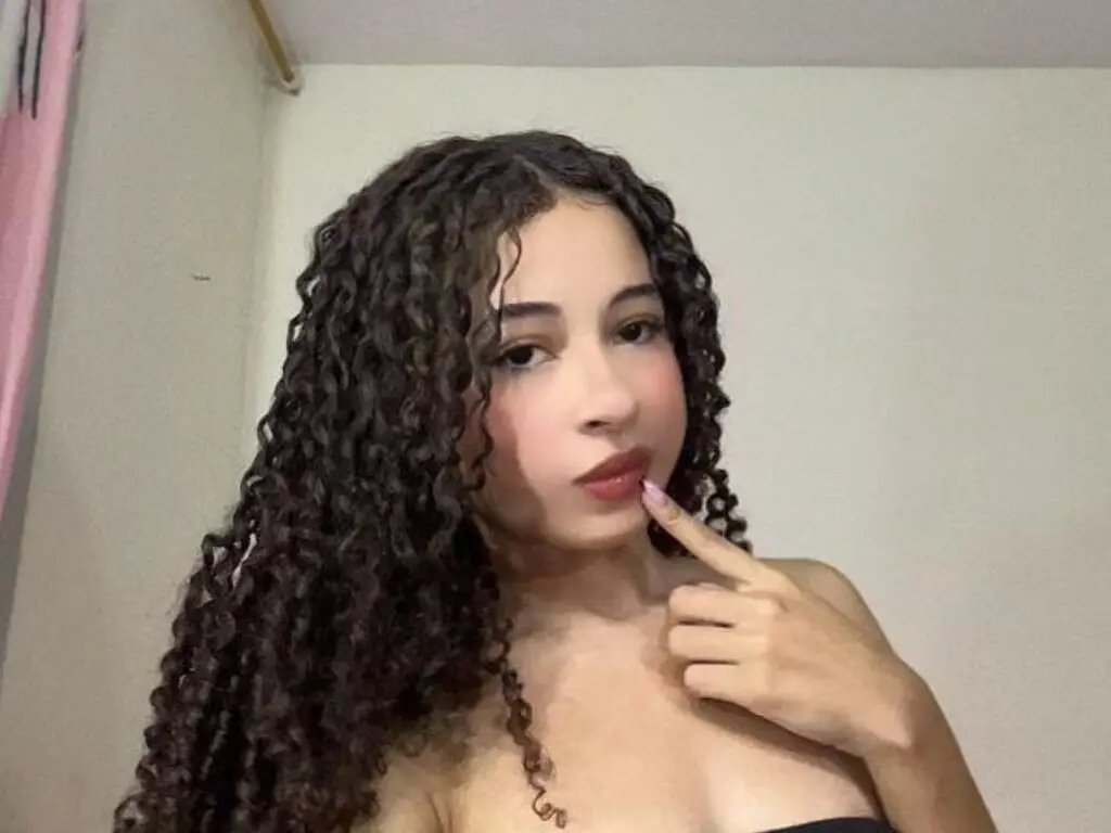 Young woman with long curly brown hair posing in a minimalist indoor setting with a soft, natural mood.