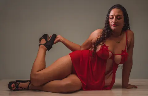Curvy woman in a red silk chemise lounging on a floor in a moody, intimate indoor setting.
