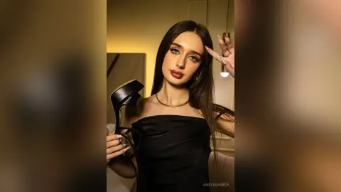 Elegant woman in a black strapless dress posing with a glamorous makeup look in a warm indoor setting.