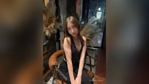 Young woman in a black sleeveless top sitting in a cozy, dimly lit cafe with dried floral decor.