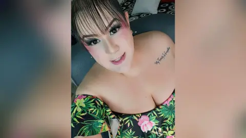 Smiling woman with bangs in a tropical floral print top relaxing on a bed in a cozy indoor setting.