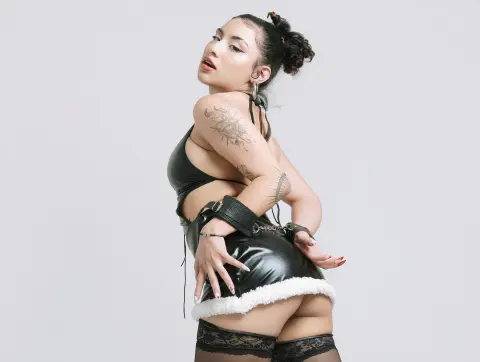 BrianaKnox — Tattooed woman in black leather mini skirt and bra posing against a white studio background.