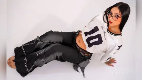 Young woman in a white San Francisco jersey and distressed black jeans posing on a white background.