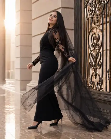 Elegant woman in a black lace evening gown with a long sheer cape standing by a classic ornate gate at sunset.