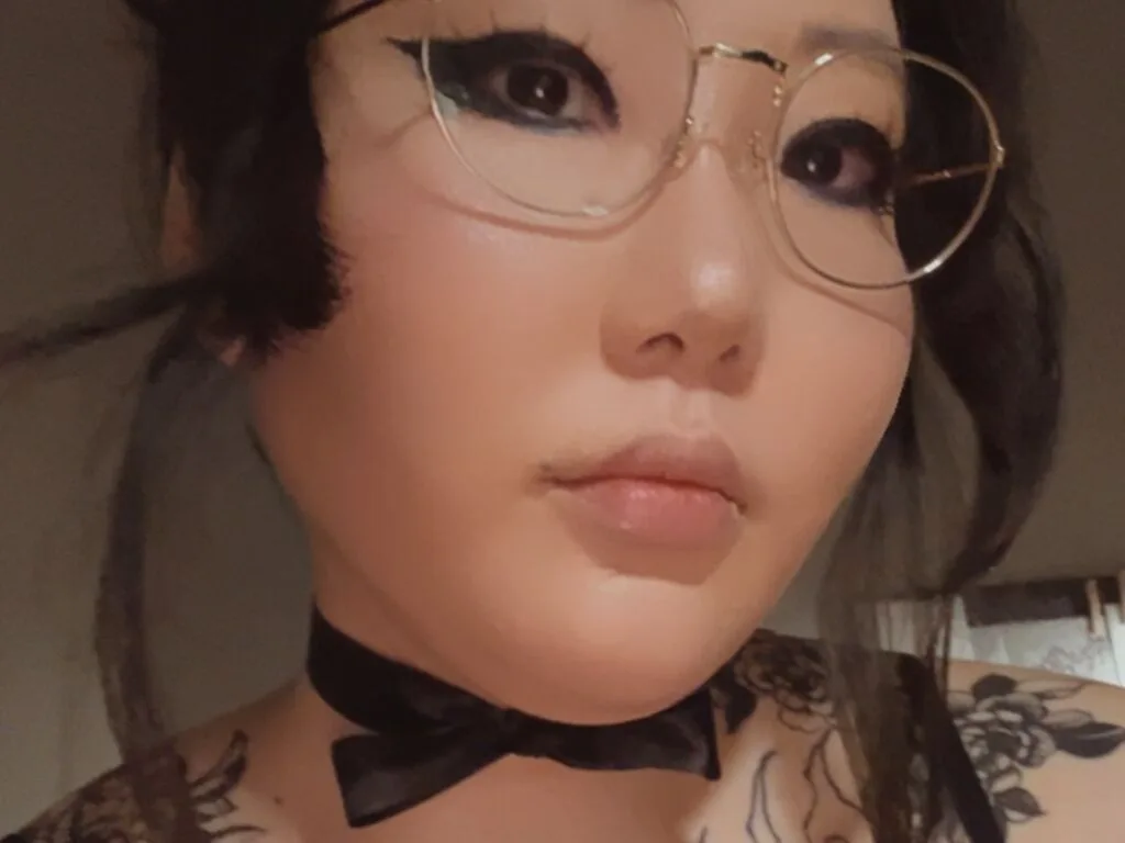 MorgueBerry — MorgueBerry wears gold-rimmed glasses and a black bow tie, looking directly at the camera with dark eye makeup.