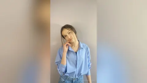 Young woman in a light blue button-down shirt posing thoughtfully against a neutral studio background.