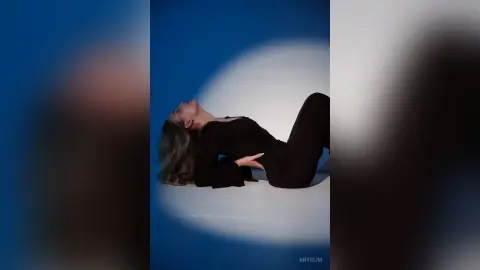 Dreamy portrait of a woman in a black long-sleeve top lying on a blue studio floor in a relaxed pose.