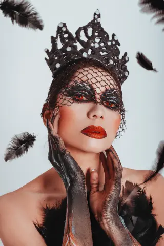 Gothic queen in black lace veil and crown with dark dramatic makeup and feathers in a moody aesthetic.