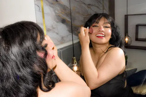Young woman in a black top applying pink blush in a modern bedroom mirror for a natural makeup look.