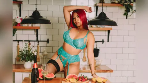 IsabellaEstrada poses in a kitchen wearing a teal lace bra and matching garter belt, showing off her red hair and bare legs.