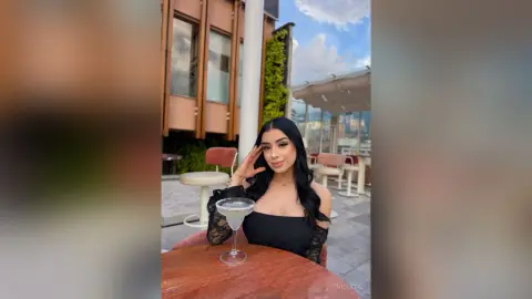 Stylish woman in a black lace top enjoying a cocktail at a sunny rooftop lounge bar.