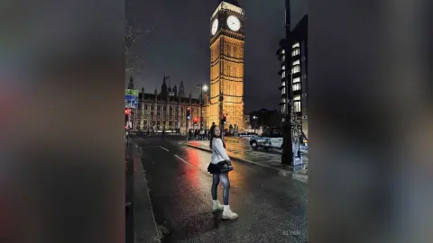 Stylish woman in a white sweater standing on a rainy London street at night near Big Ben.