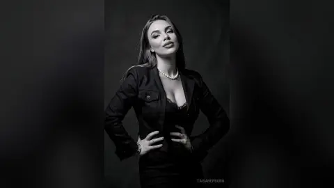 Elegant woman in a black blazer and lace top posing confidently in a moody black and white studio portrait.
