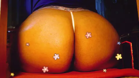 Close-up of a woman's tan skin in floral patterned underwear sitting on a red surface in warm lighting.