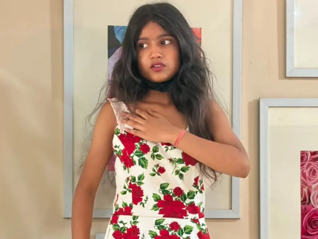 PihuPriya with long dark hair wearing a white floral sundress, posing in front of a framed picture.
