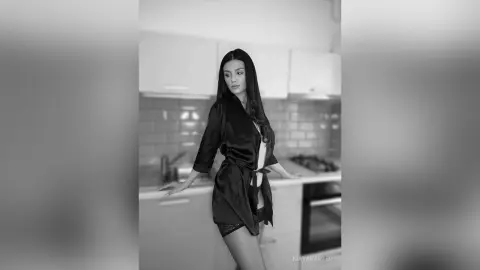 Elegant woman in a black silk robe posing in a modern kitchen, moody black and white portrait.