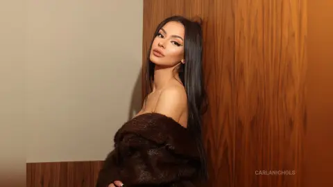 Elegant woman in a luxurious brown faux fur coat posing against a wooden wall with a moody, sophisticated vibe.