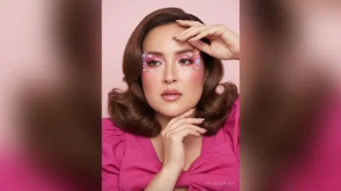 Glamorous woman with vintage wavy hair and floral eye makeup wearing a bright pink blouse against a soft pink backdrop.