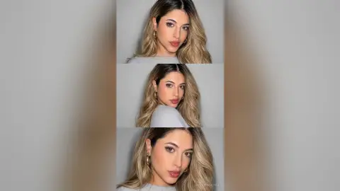 IrinaMolkova poses with long blonde hair and gold hoop earrings, wearing a grey top against a plain background.