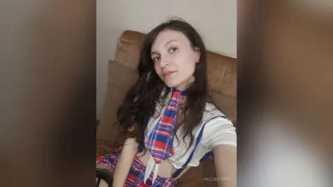 Young woman in a white and red plaid schoolgirl outfit sitting on a couch with a relaxed expression.