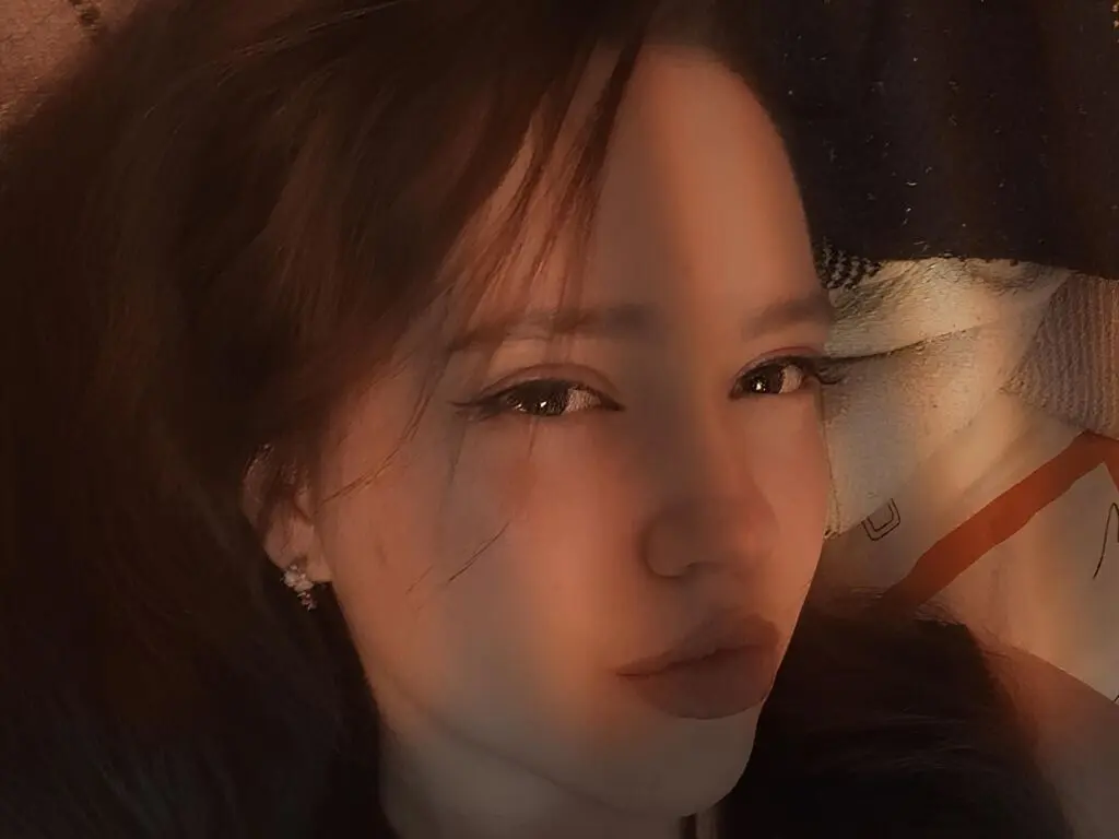Close-up portrait of a young woman with long hair in warm, moody indoor lighting.