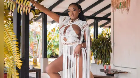 Confident woman in a white macramé cutout bodysuit posing in a tropical outdoor patio setting.