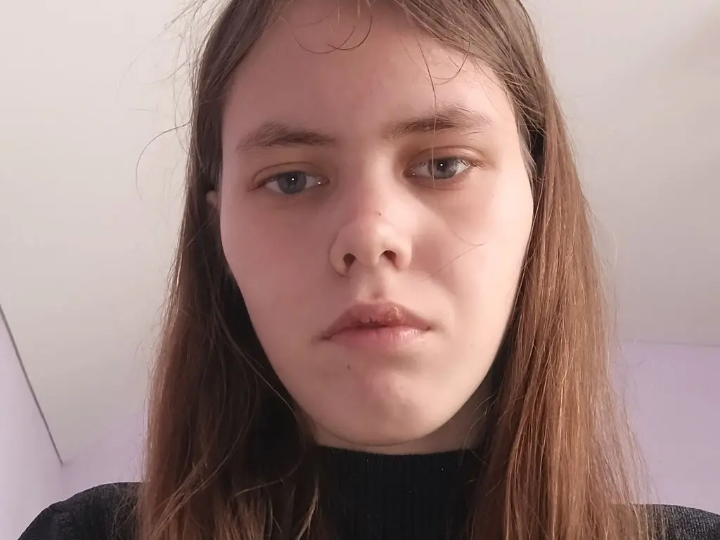 Close-up portrait of a young woman with long brown hair wearing a black turtleneck in a soft indoor setting.