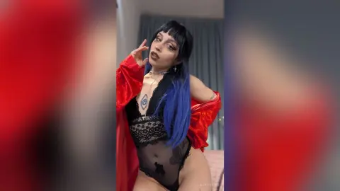Woman with blue hair in black lace bodysuit and red robe posing in a bedroom setting.