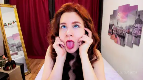 Redheaded woman making a playful face in a cozy room with vintage decor and warm lighting.