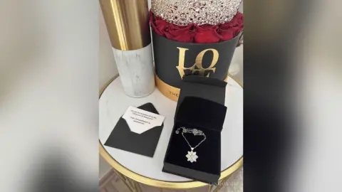 Luxury gift set featuring a red rose box, a silver star pendant necklace, and a romantic note on a marble table.