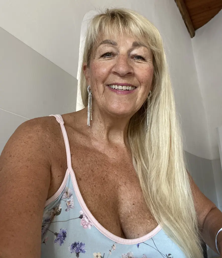 FoxyLeo smiles while posing close-up, showing her blonde hair and cleavage in a black top.