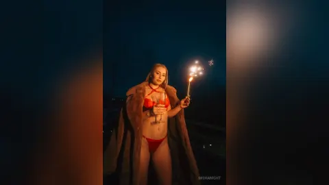 MishaNight — MishaNight wears red lingerie and a fur coat while holding a sparkler and a drink at night.