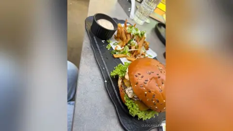 Delicious gourmet cheeseburger and crispy french fries served with dipping sauce on a black platter in a restaurant.
