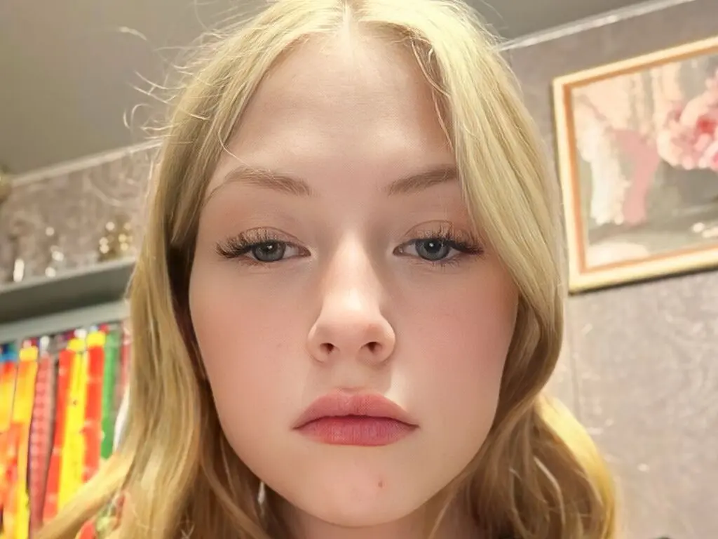 Close-up portrait of a blonde woman with natural makeup looking calmly at the camera in a bright indoor setting.