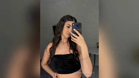 CatherineThomase — CatherineThomase takes a mirror selfie wearing a black velvet tube top and showing her long wavy hair.