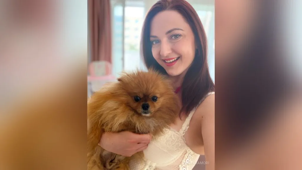 VarvaraMori — VarvaraMori smiles while holding a fluffy brown Pomeranian dog in her arms.