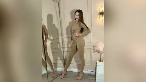 Elegant woman in a beige long-sleeve bodysuit posing in a modern minimalist room with a full-length mirror.