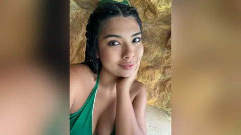 Smiling young woman in a green halter top posing against a natural rock wall background.
