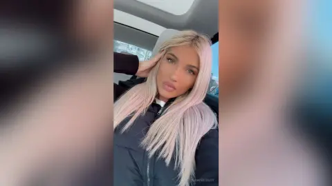 Blonde woman in a black puffer jacket posing with a relaxed expression inside a car.
