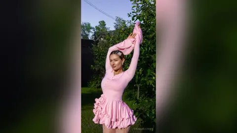 Young woman in a pink ruffled dress posing outdoors in a lush green garden during golden hour.
