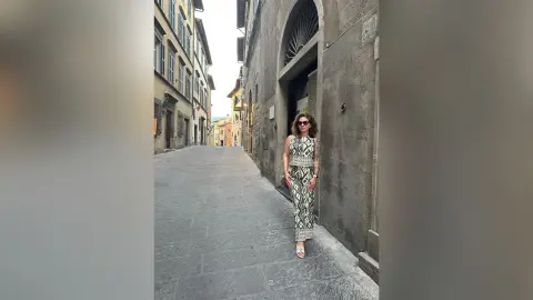 Stylish woman in a black and white patterned maxi dress walking down a narrow European cobblestone street.