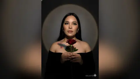 Elegant woman in a black off-the-shoulder top holding a red rose in a moody, cinematic studio portrait.